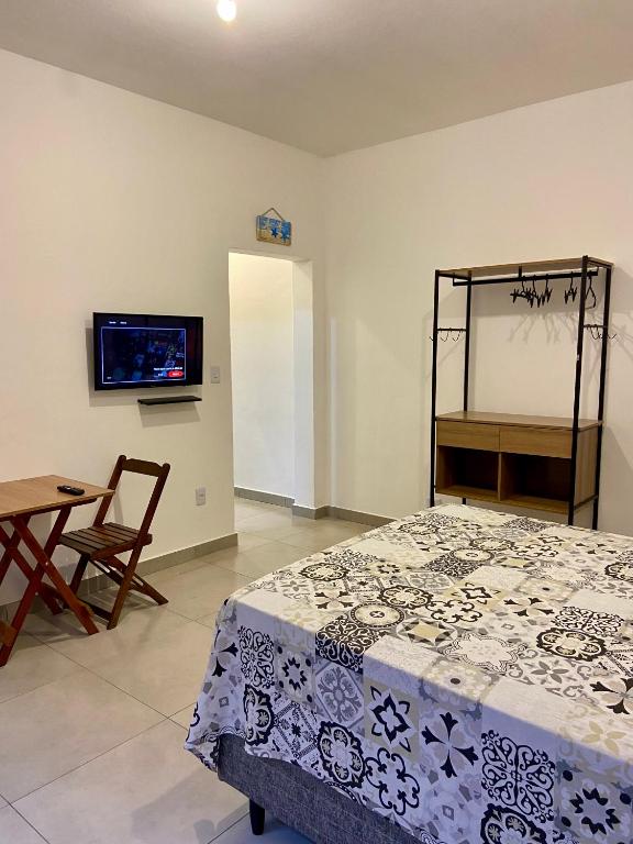 a bedroom with a bed and a table and a tv at Suítes Itapoã in Ubatuba