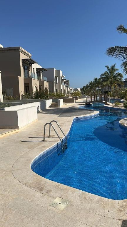 a swimming pool in a resort with palm trees and buildings at Cosy 1BR with a PUBLIC POOL and WIFI in Ma‘mūrah