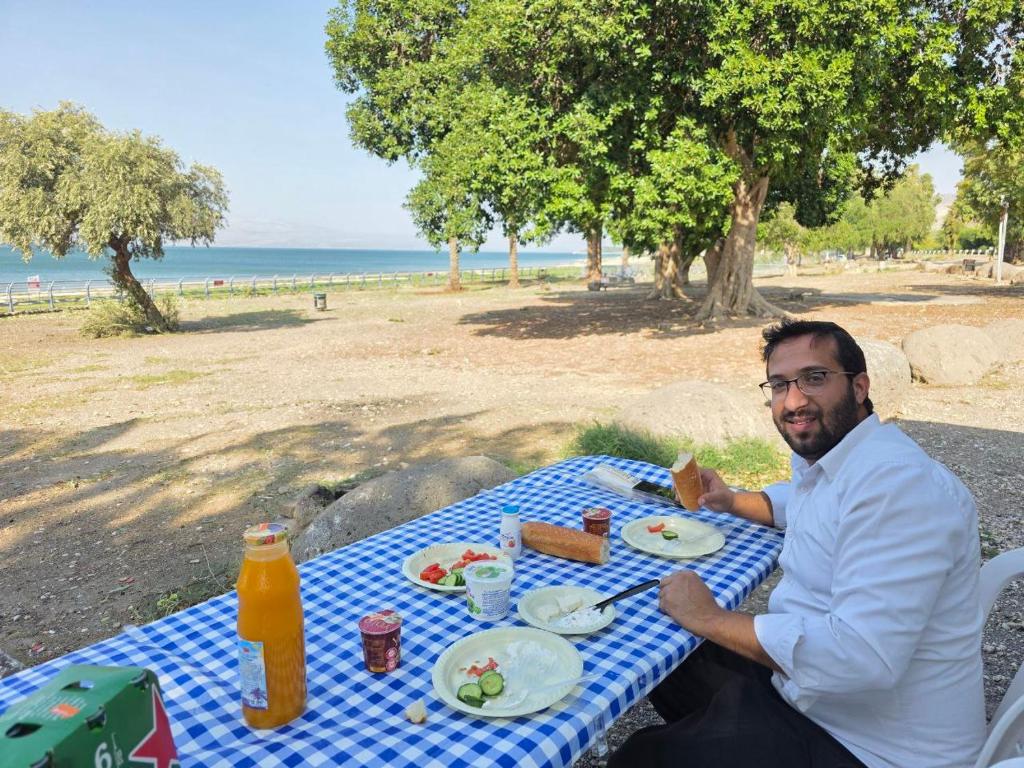 a man sitting at a picnic table at the beach at רויאל וואן in Tiberias