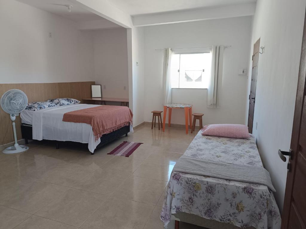 a bedroom with two beds and a table and a window at Kitnet amplo in Santa Cruz Cabrália
