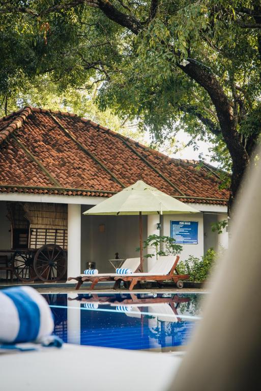 a pool with a table and an umbrella next to a house at Gimanhala Hotel in Dambulla