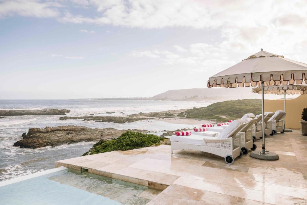 eine Terrasse mit Stühlen, einem Sonnenschirm und dem Meer in der Unterkunft Birkenhead House in Hermanus