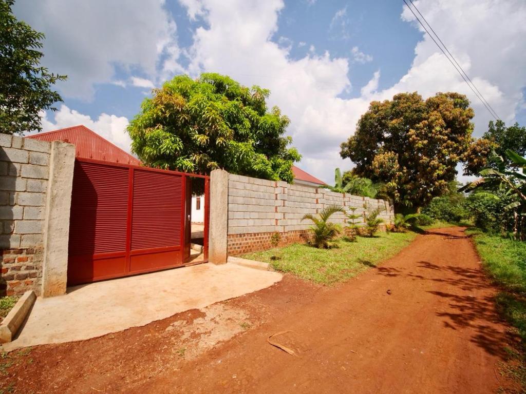 a building with a red door next to a dirt road at Nile River Inn in Buloba