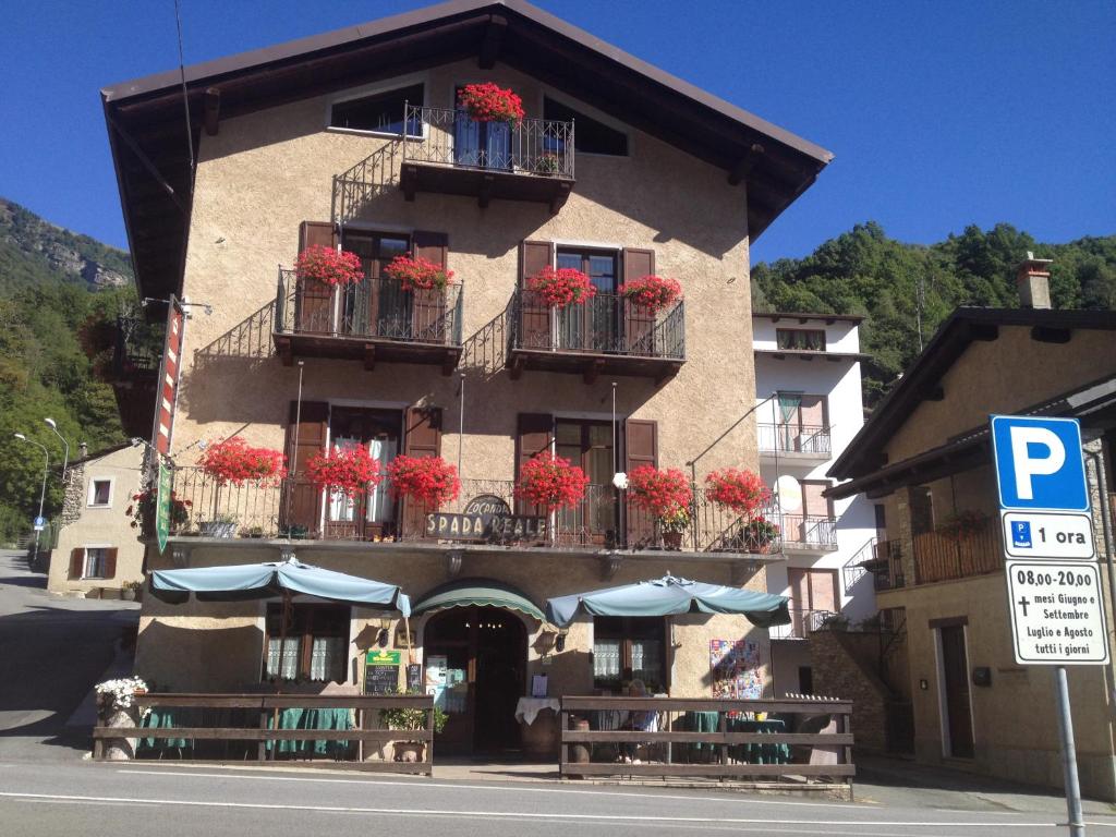 um edifício com flores vermelhas em varandas com mesas e guarda-sóis em Locanda Spada Reale em Frassino