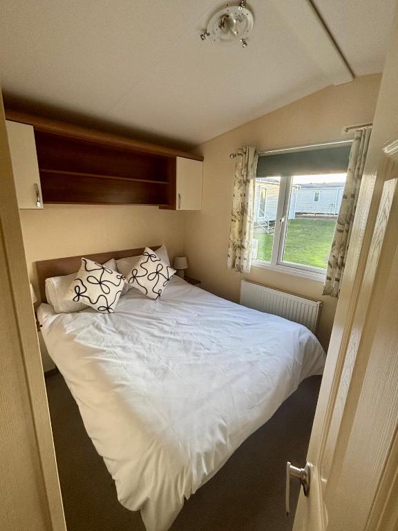 a bedroom with a white bed with pillows and a window at Relax By The Coast - Spacious 6-sleeper Caravan in Leysdown-on-Sea