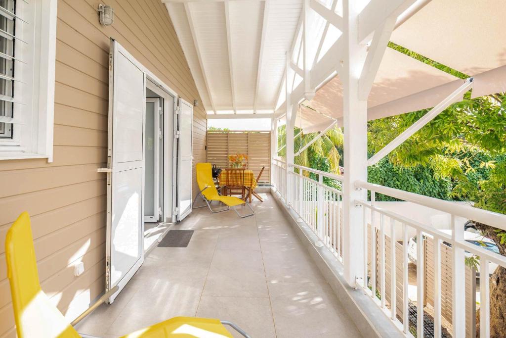 a screened porch with yellow chairs and a table at Villa Le Manguier - Logement Marcus, Tout Confort in Goyave