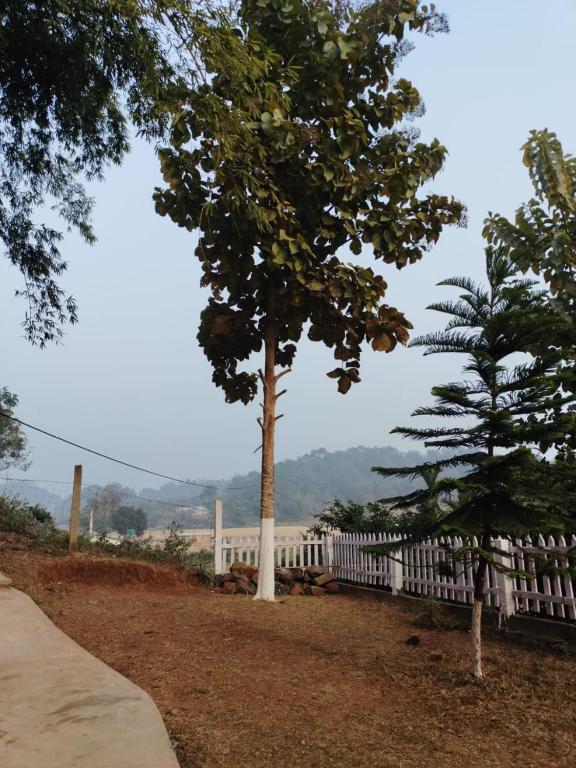 two trees next to a white fence at Mur Farm House in Sonāpur