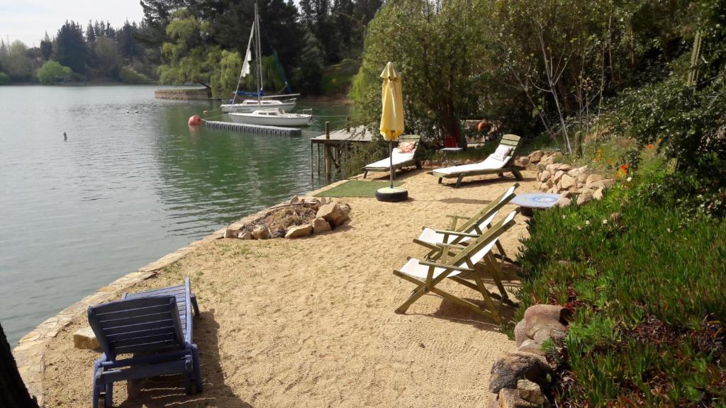 un gruppo di sedie e un ombrellone sulla riva di un lago di Cabaña de Adobe en Lago Rapel a Lago Rapel