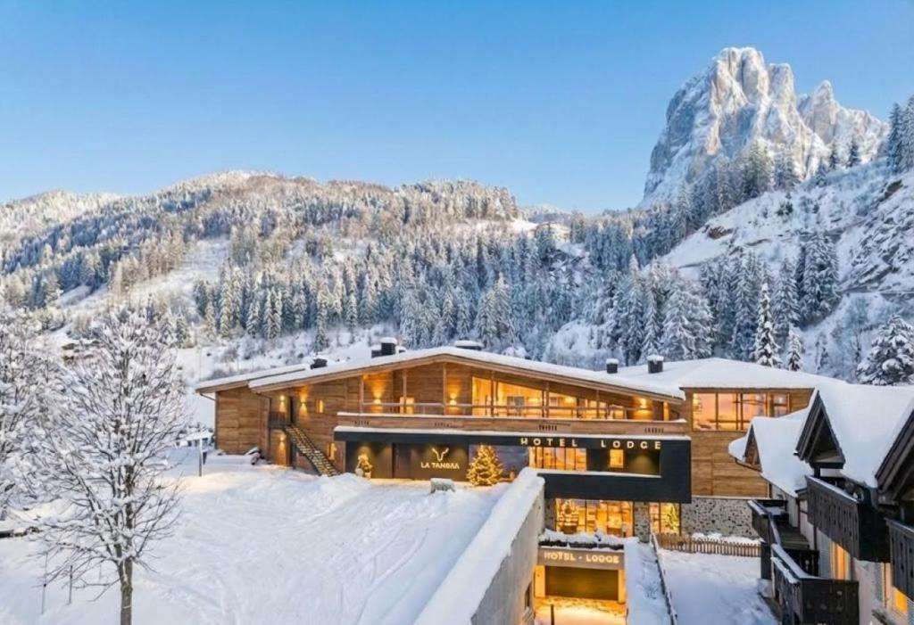 a house in the snow with mountains in the background at La Tambra - Hotel Lodge in Santa Cristina in Val Gardena