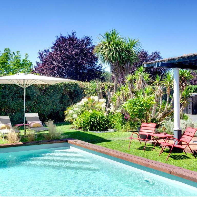 a swimming pool in a yard with chairs and an umbrella at 3 chambres d'hôte de charme et chambre de luxe indépendante Ô Bois Plage in Gujan-Mestras