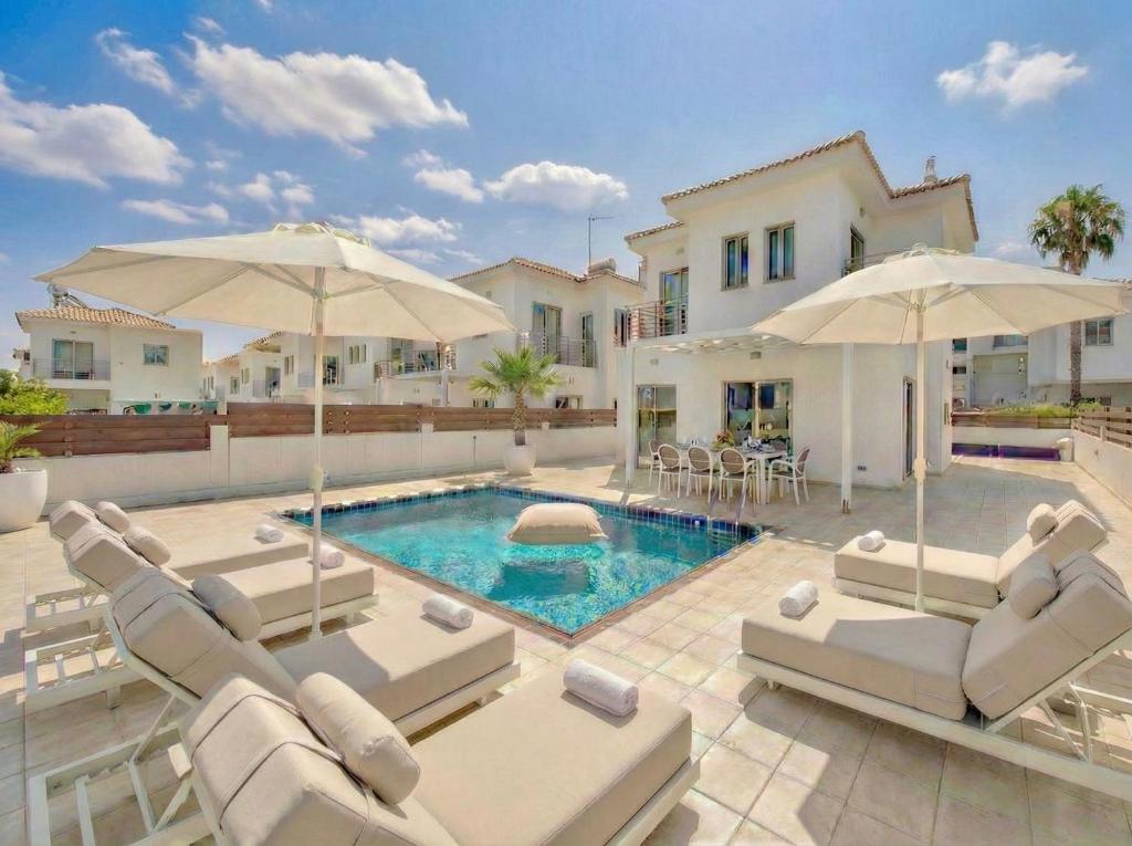 a villa with a swimming pool with chairs and umbrellas at Fig Tree Beach Villa Two in Paralimni