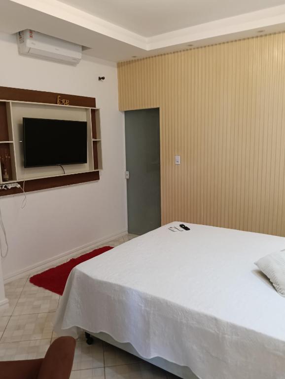 a bedroom with a white bed and a flat screen tv at Sítio Moriá in Camaçari