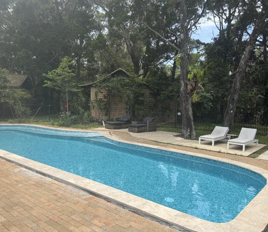 a swimming pool with two chairs and a table at Byron Bay Rainforest Resort in Byron Bay