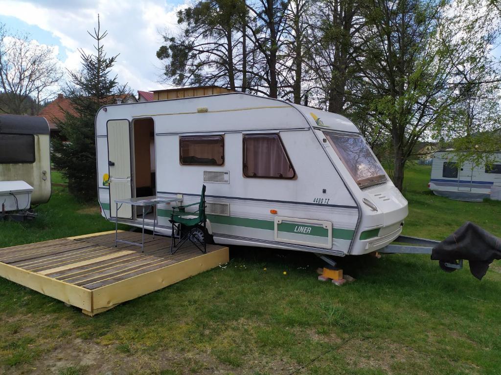 a white caravan parked in a field with a deck at Dobromil - Camp pod kaštany in Morávka