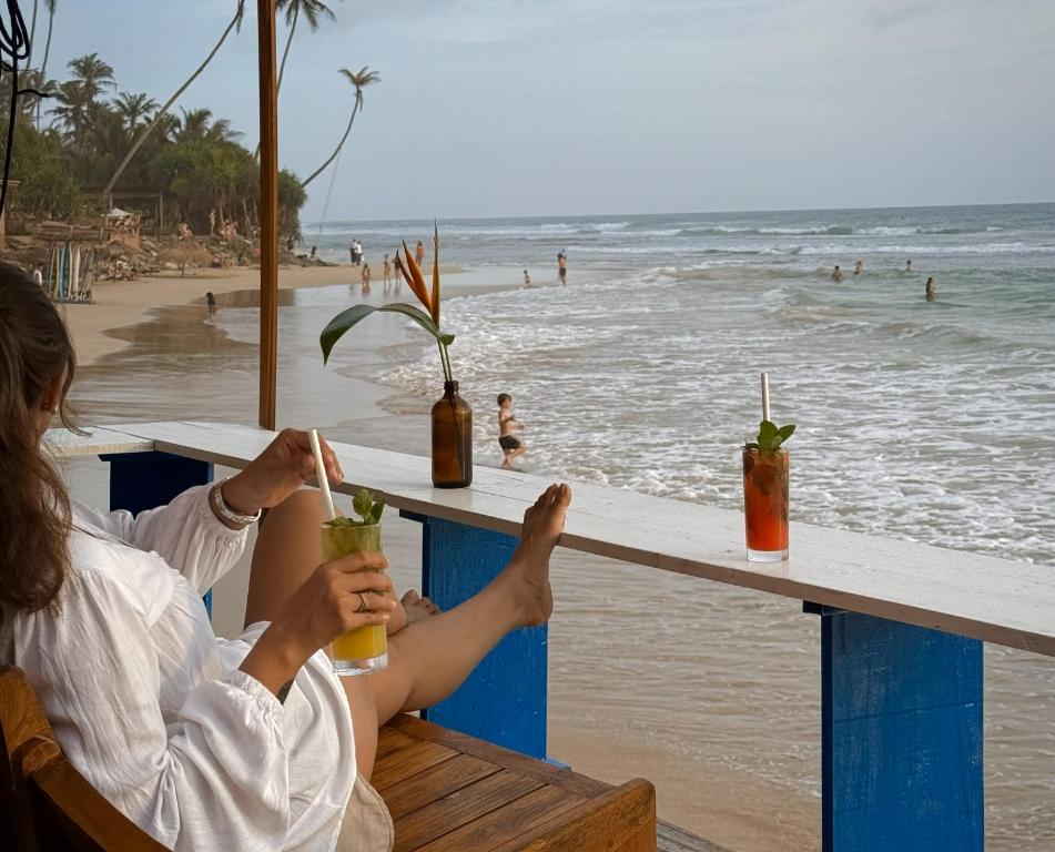 a woman sitting at a bar on the beach with drinks at Pelican Ahangama in Ahangama