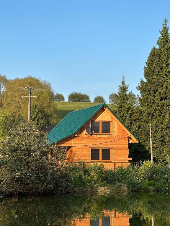 a wooden cabin with a green roof next to a lake at Koński Zakątek in Lutowiska