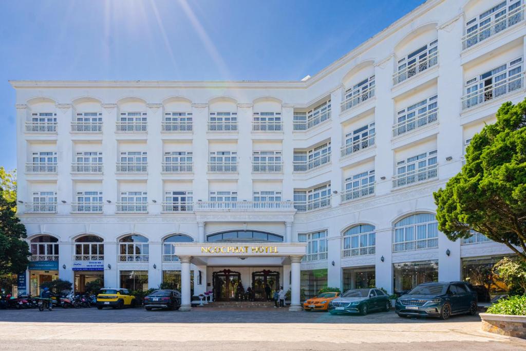 un grande edificio bianco con le auto parcheggiate di fronte di Ngoc Phat Dalat Hotel a Da Lat