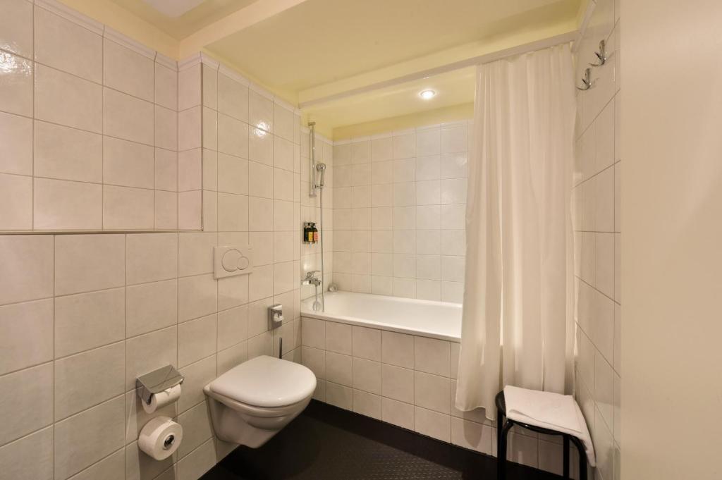 a white bathroom with a toilet and a bath tub at Romantik Hotel Schwan in Horgen