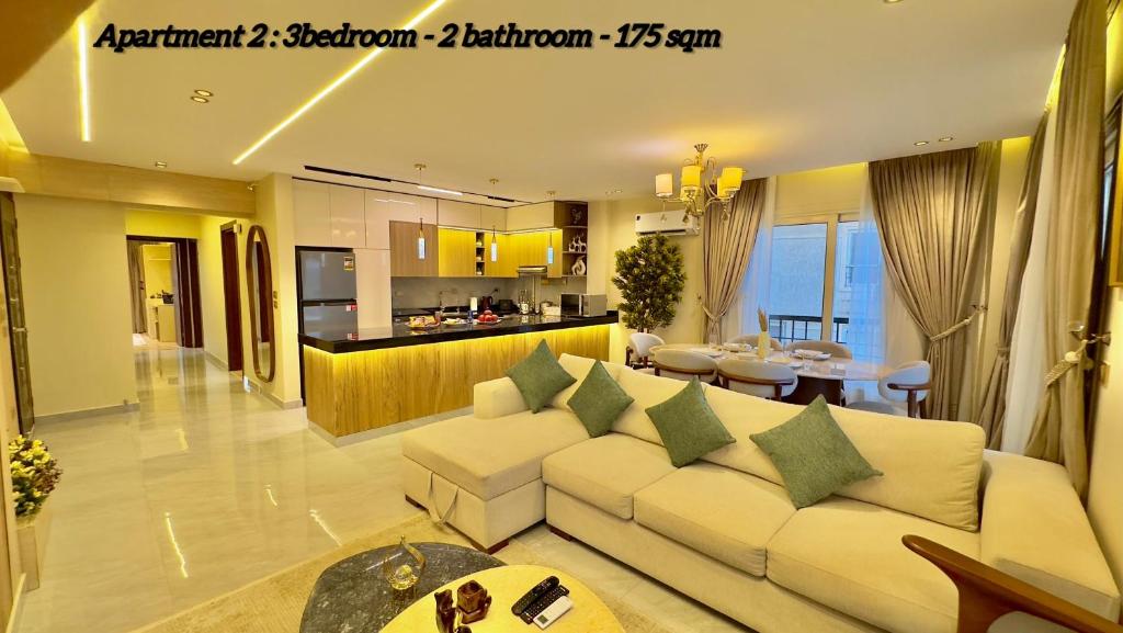 a living room with a white couch and a kitchen at Ultra Luxury 3BR with Pools ,Sports ,Dining in Gated compound, Close to all sites in Cairo