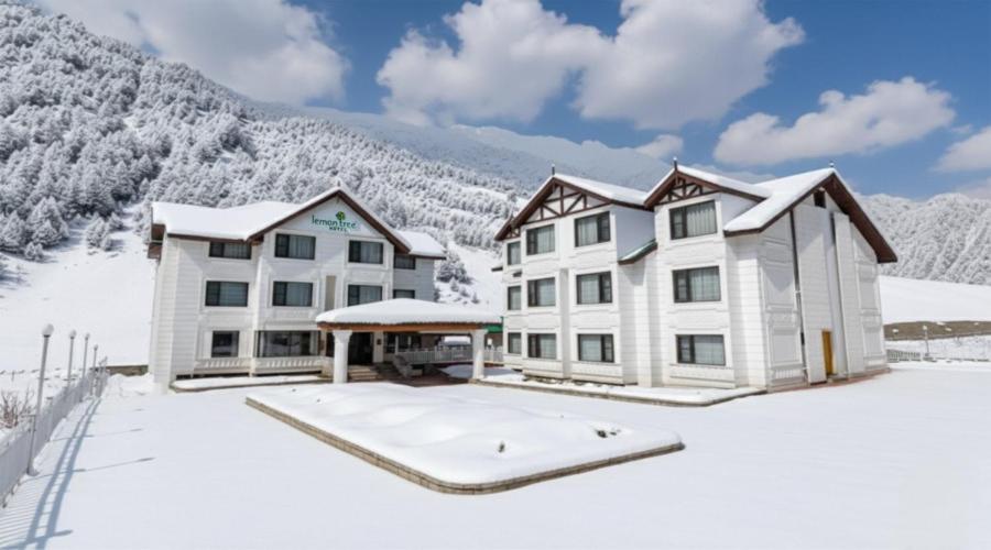 a house in the snow with mountains in the background at Lemon Tree Hotel, Sonmarg by the Riverside in Sonāmarg