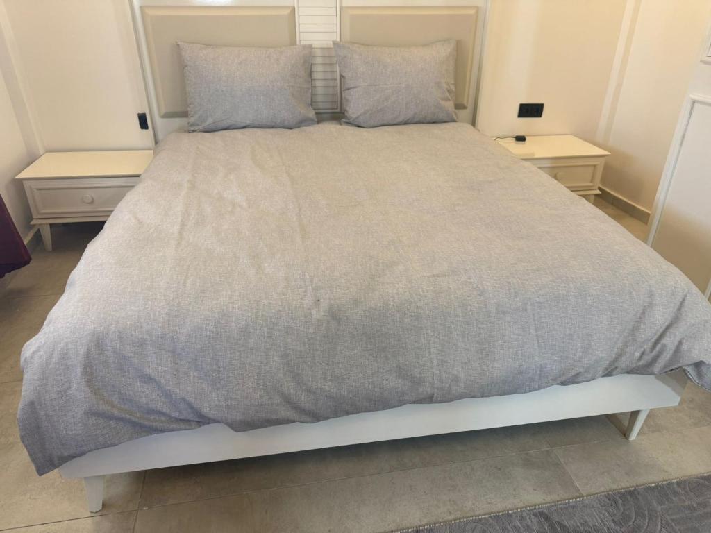 a bed with a gray comforter and two tables at Harran Kümbet Otel in Harran