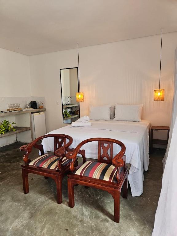 a bedroom with a large bed with two chairs at Casa Entre Coqueiros in Tamandaré