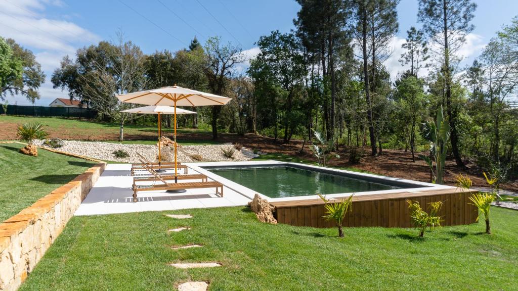 a pool in a yard with an umbrella and a bench at Quinta Sra do Carmo in Ferreira do Zêzere