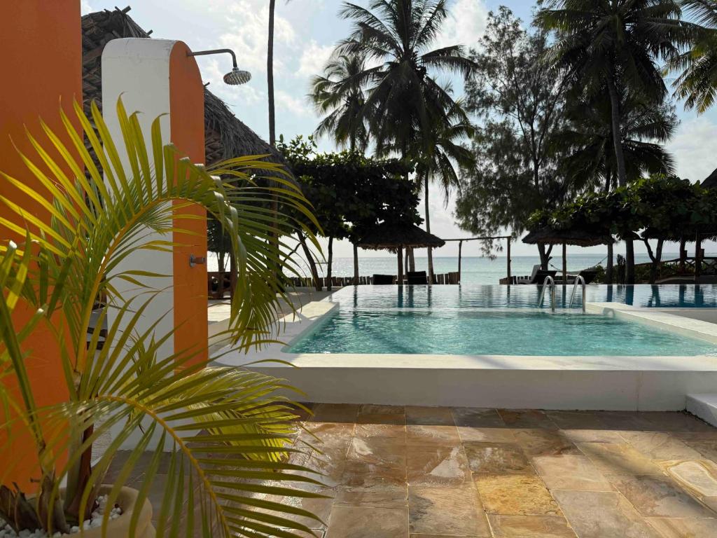 a swimming pool with palm trees and the ocean at Amani Palms by Manolo Beach Resort in Uroa