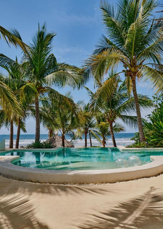 a swimming pool on a beach with palm trees at Casablanca Escape in La Majahua