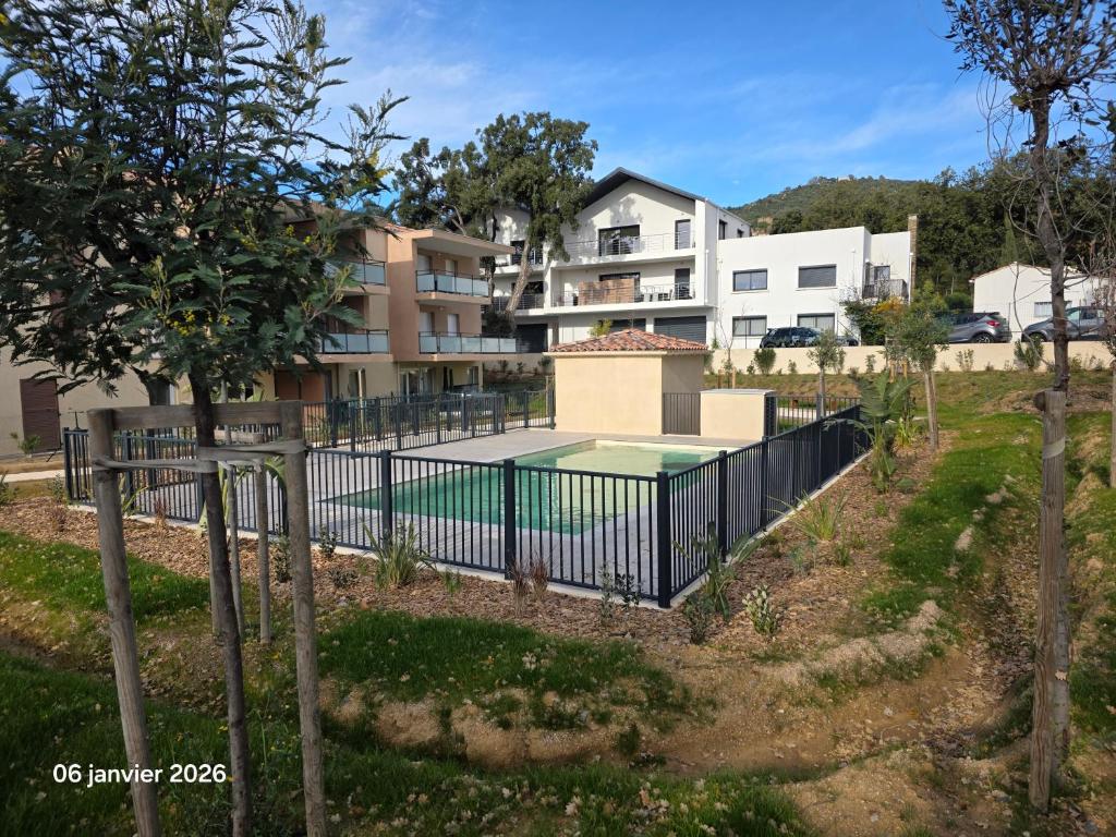 a fence with a tennis court in front of a building at Spacieux appartement dans résidence avec piscine in Bormes-les-Mimosas