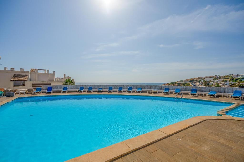 a large swimming pool with blue chairs and the ocean at Ocean View - XL Terrace - Beachfront by Tenório in Lagos