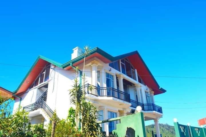 a white building with a balcony and palm trees at Hill Paradise Nuwaraeliya in Nuwara Eliya