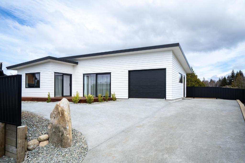 a white house with a black garage at Murchison View house with Jacuzzi in Te Anau
