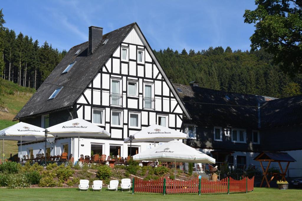 ein großes schwarzweißes Gebäude mit Tischen und Sonnenschirmen in der Unterkunft Hotel & Restaurant Forellenhof in Bad Berleburg