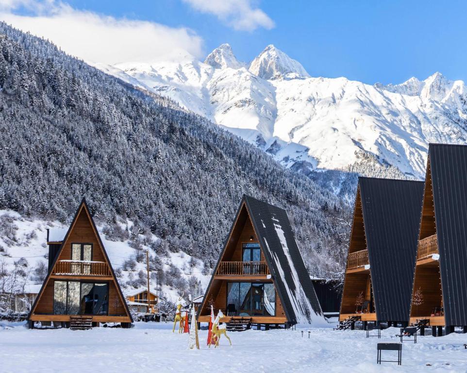 a group of buildings in the snow with mountains in the background at Winterfell Mestia - Premium Chalet Complex & SPA in Mestia