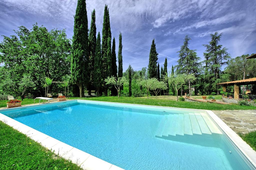 ein großer blauer Pool in einem Garten mit Bäumen in der Unterkunft Villa Lo Scoiattolo by PosarelliVillas in Subbiano
