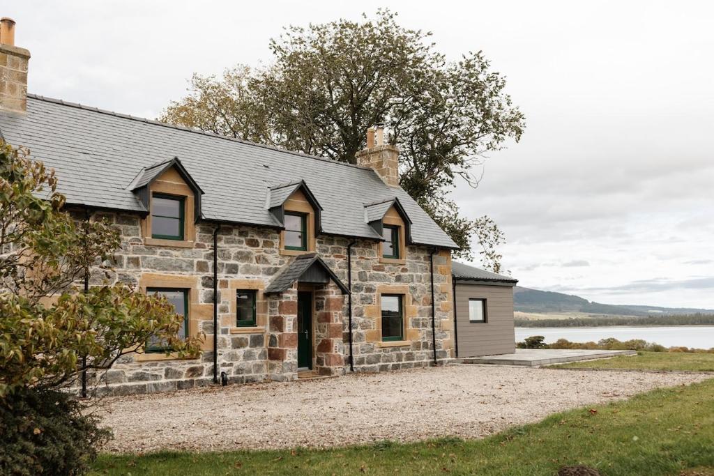 an old stone house with a lake in the background at Luxury Farmhouse, near Dornoch in The Mound