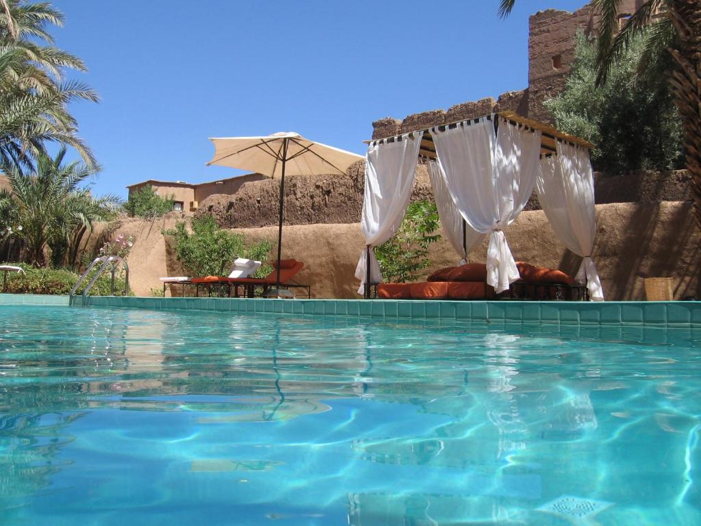 een zwembad met een bed en een parasol bij Dar Qamar in Agdz