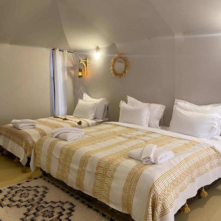 a bedroom with two beds with white pillows and a mirror at Sunshine luxury desert camp in Merzouga