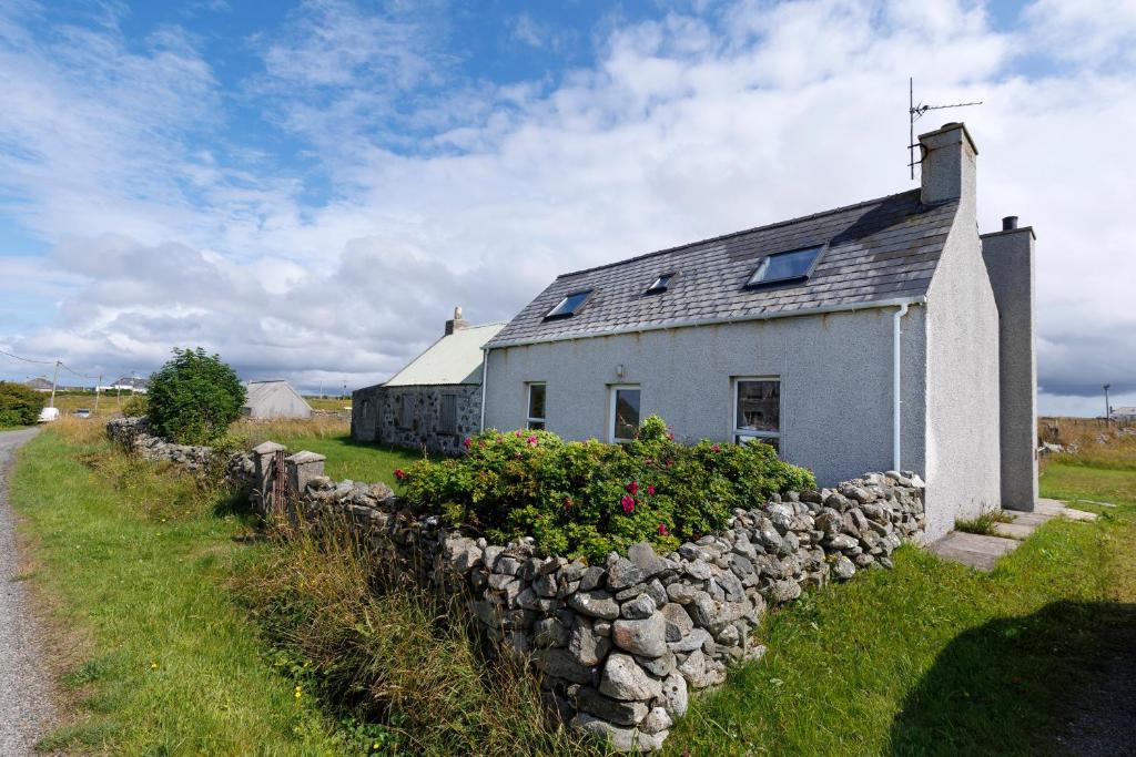 a white house with a stone wall next to a road at Cosy Croft in Lower Shader