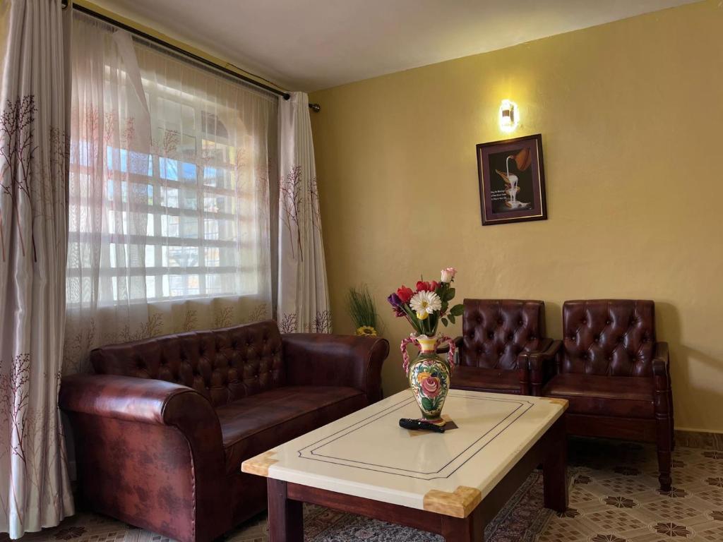a living room with two leather couches and a table with flowers at Golf BnB in Nyahururu