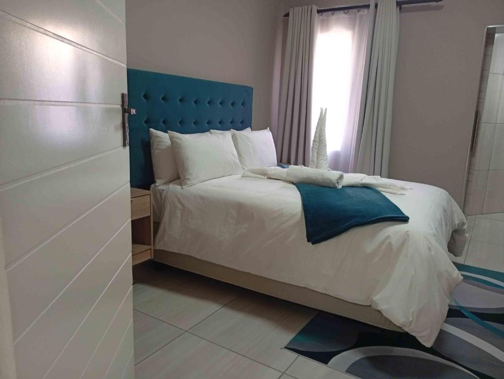 a bedroom with a bed with a blue headboard and a window at Joyful Home Bela-Bela in Bela-Bela