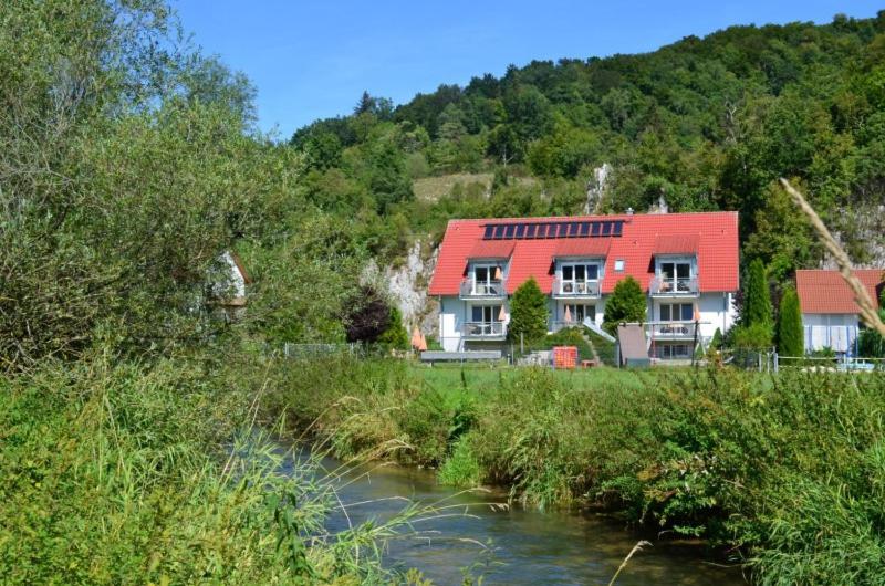 a house with a red roof next to a river at Ferienwohnungen Holder in Anhausen