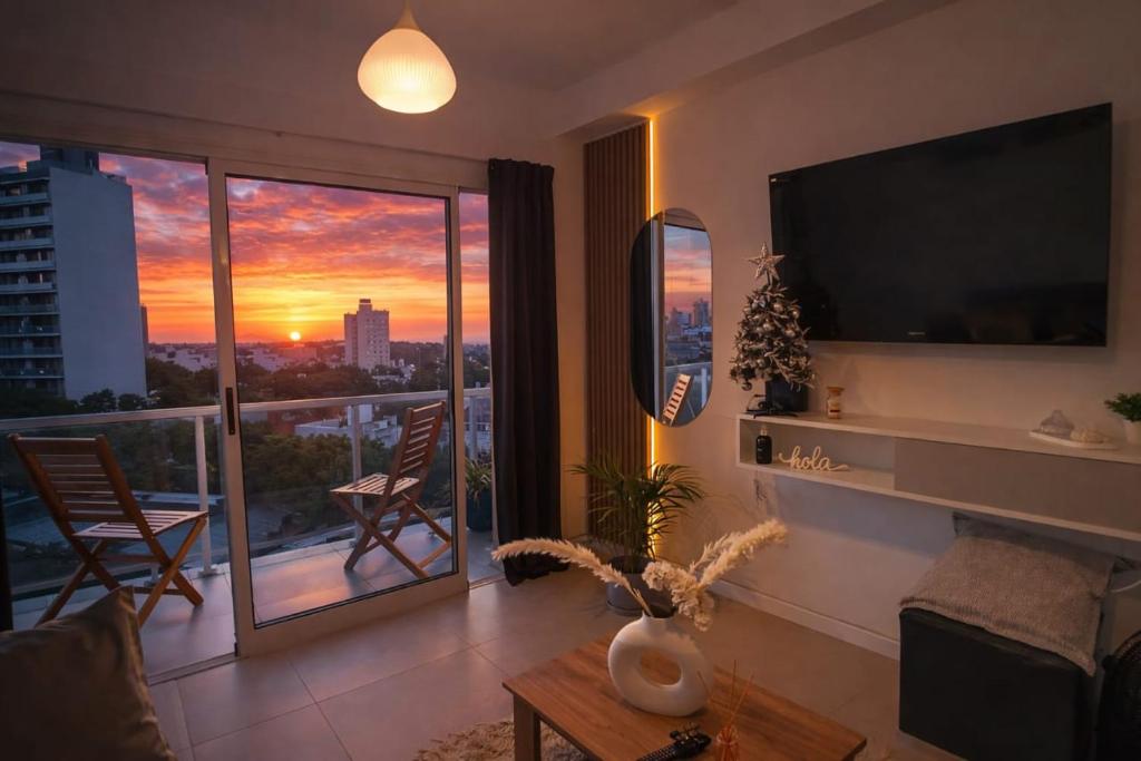 a living room with a television and a balcony with a sunset at Apart Alameda in Paraná