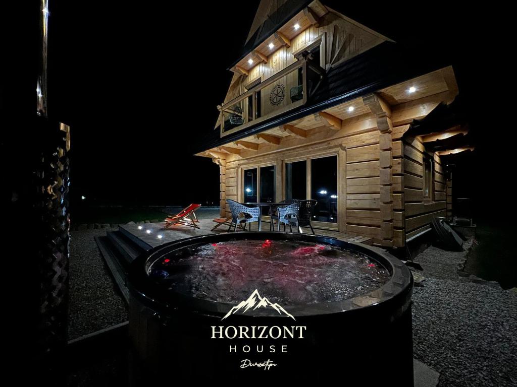 a hot tub in front of a house at night at Horizont House - domki z prywatnymi baliami oraz ogólnodostępną sauną - IZBY PODHALAŃSKIE in Dursztyn