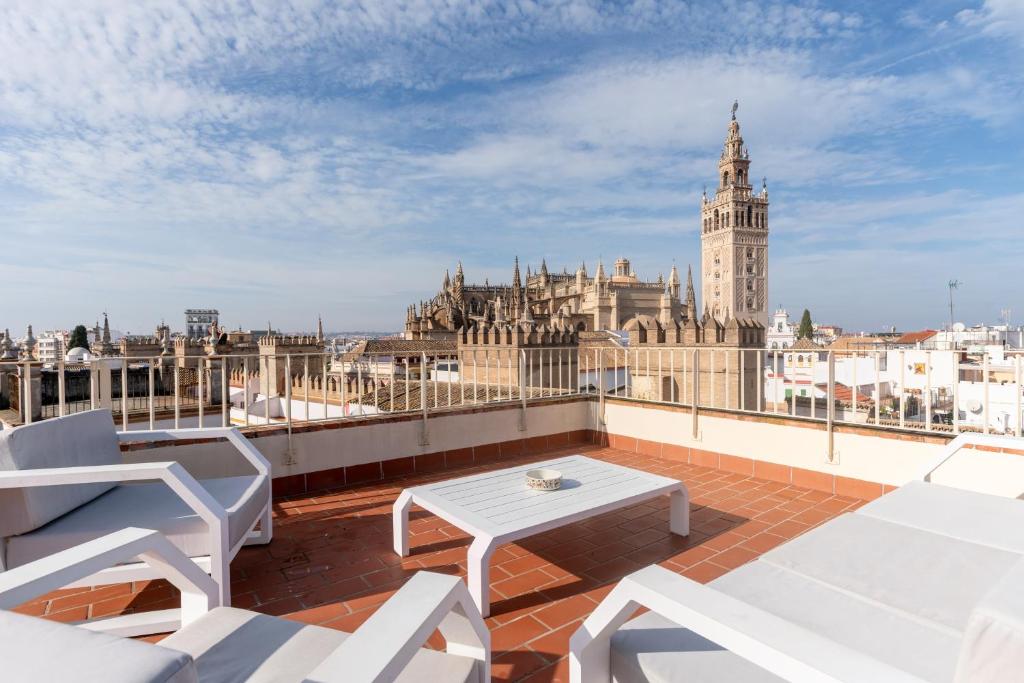 a balcony with white chairs and a table and a clock tower at Puerta Principe Luxury Apartments in Seville