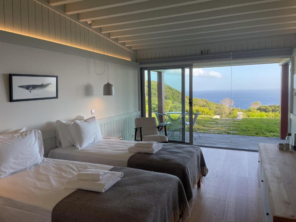 two beds in a room with a view of the ocean at Abrigos Baleeiros Turismo Rural in Feiteira