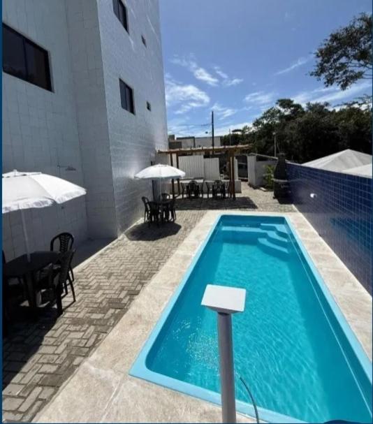 a swimming pool next to a building with tables and umbrellas at Lisboa in João Pessoa