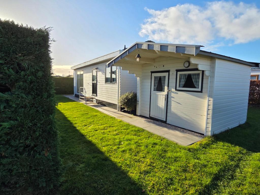 a white shed with a door on a lawn at Chalet Zon & Zee in Zonnemaire