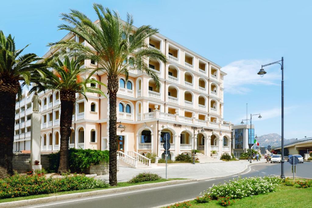 a large white building with palm trees in front of it at Grand Hotel President in Olbia
